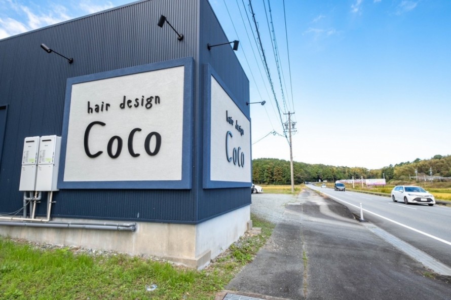 道路沿いに設置されたカルプ文字の大きな黒い看板がある美容院