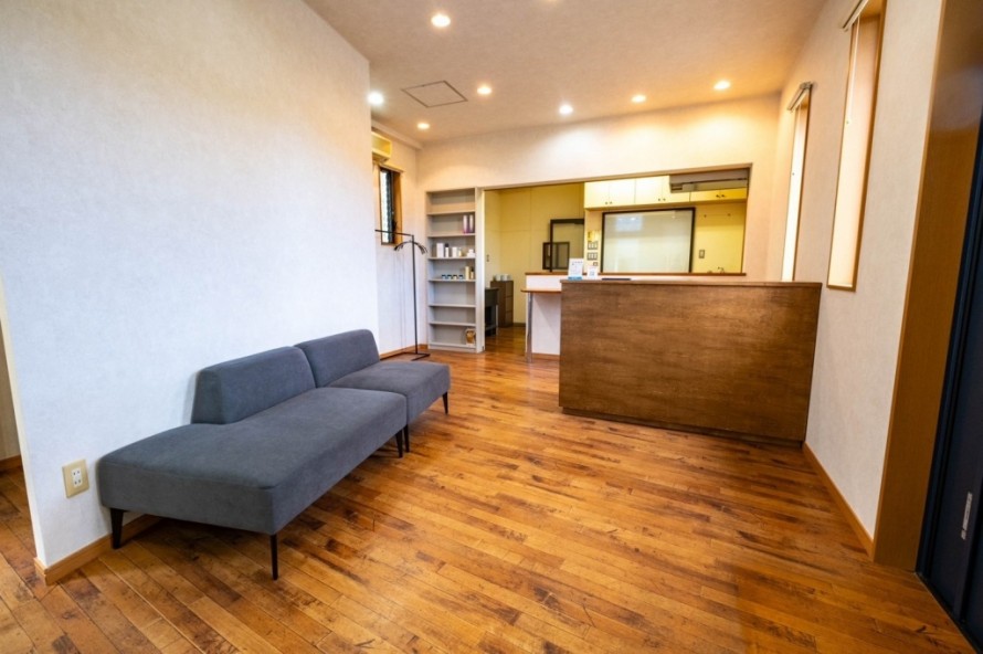 木目カウンターとグレーのソファを配置した美容院の受付待合スペース