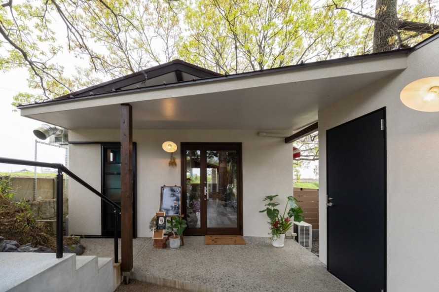 白い塗り壁と木製柱が特徴の隠れ家カフェの入口デザイン