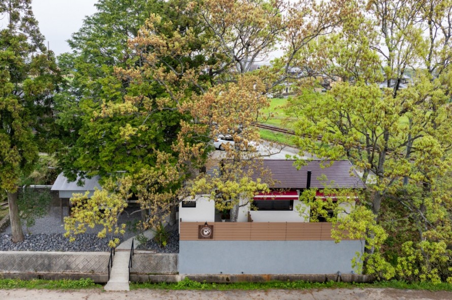 木々に囲まれた白い外壁と木目フェンスの隠れ家カフェ外観