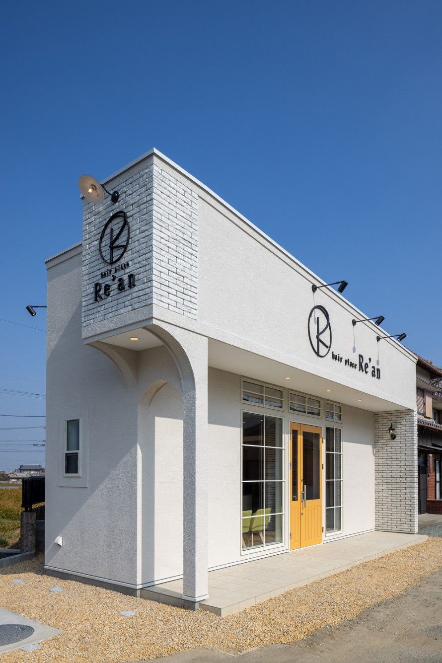 美容院の昼間の外観。白壁にレンガとカルプ文字を使用した店舗外観