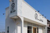 美容院の昼間の外観。白壁にレンガとカルプ文字を使用した店舗外観